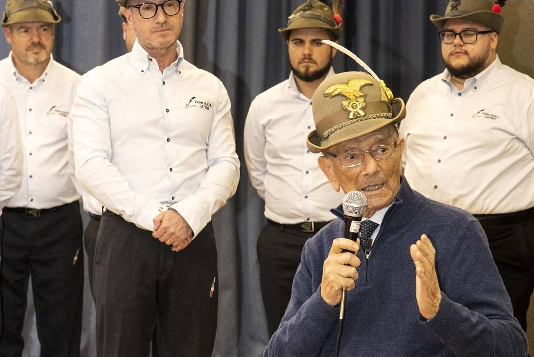 Il Maggiore Francesco Totaro con il cappello alpino interviene al microfono, con i coristi alle spalle
